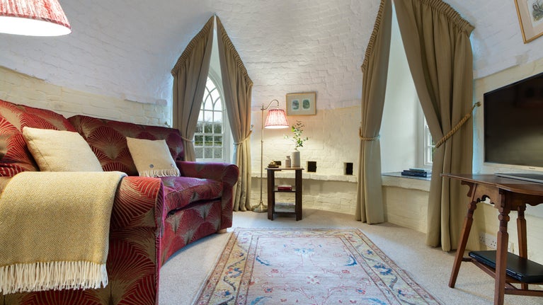 The sitting room at Trelissick Water Tower, a circular room with curved sofa and two arched windows, Cornwall